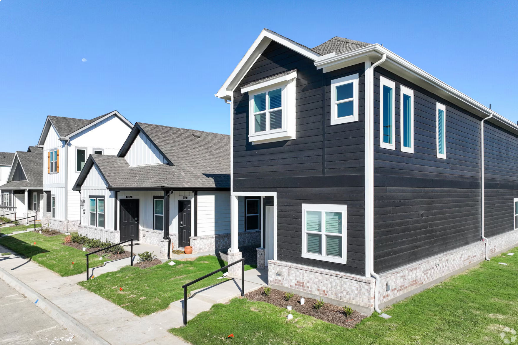Row of houses with dark gray siding and white trim on a clear day.